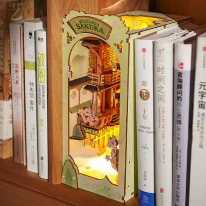 Book Nook Falling Sakura installé sur une vraie étagère de nuit, éclairage LED chaud entre les livres