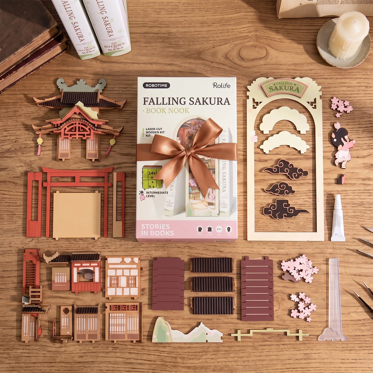 Vue éclatée des pièces en bois précoupées du Book Nook Falling Sakura avec la boîte d'origine Robotime Rolife et le ruban cadeau