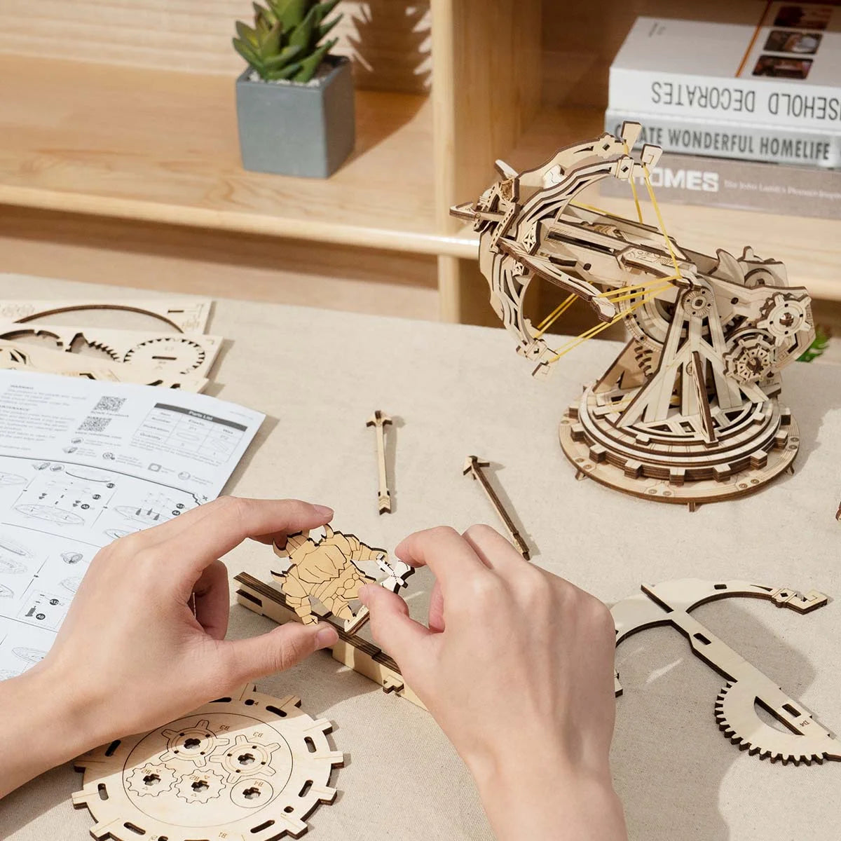Mains assemblant la figurine du kit baliste en bois sur un bureau