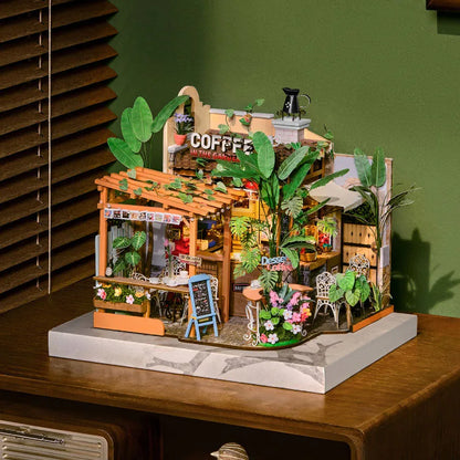 Maison miniature Leafree Café exposée sur un socle blanc, mur vert en fond