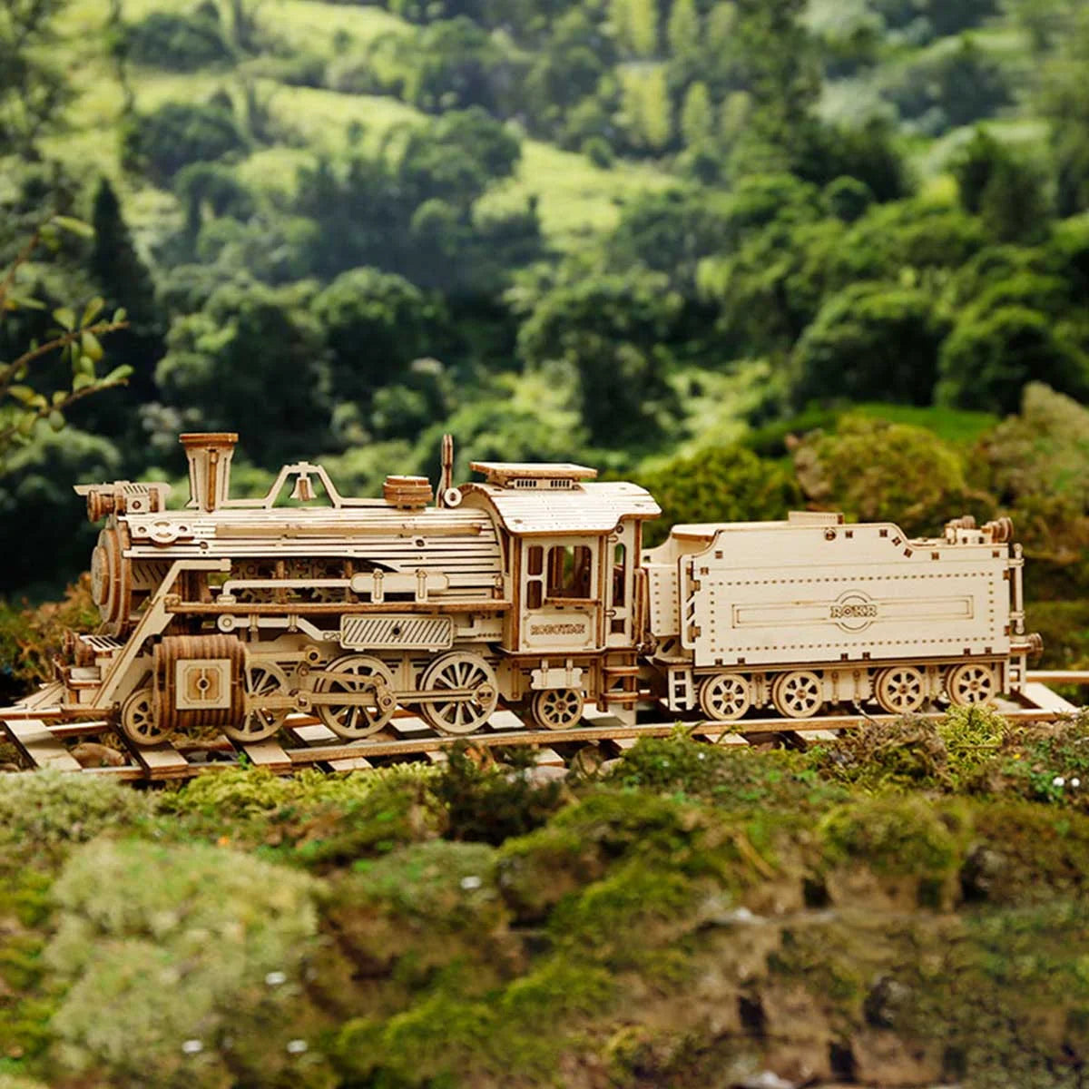 Locomotive à vapeur en bois et son tender sur une voie dans un paysage vert