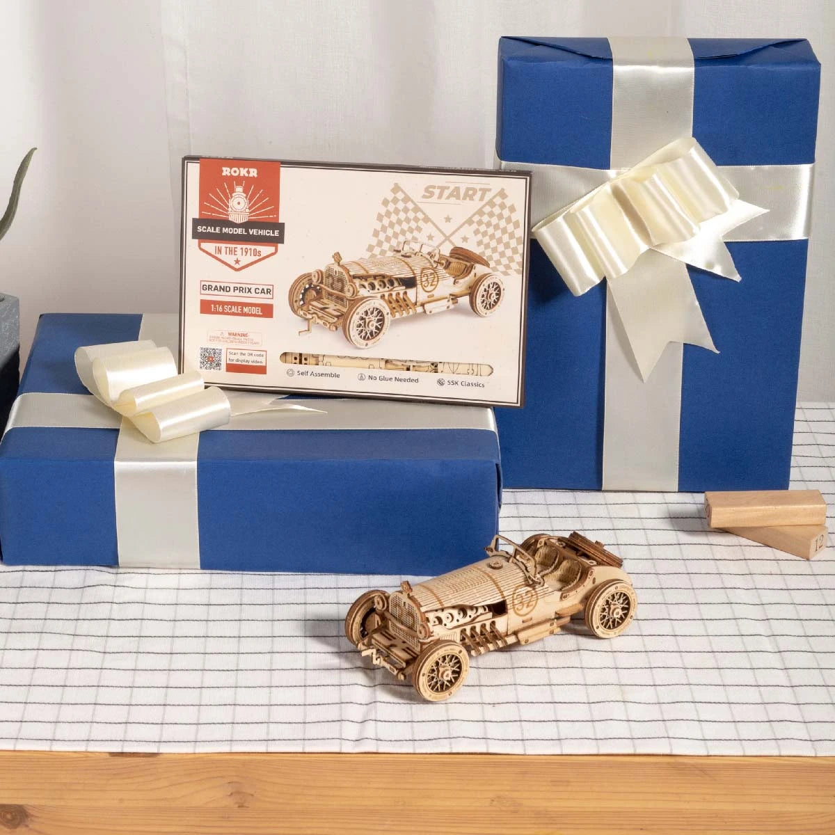Coffret d'origine de L'Héritage Automobile entre deux paquets cadeaux, maquette en bois assemblée devant