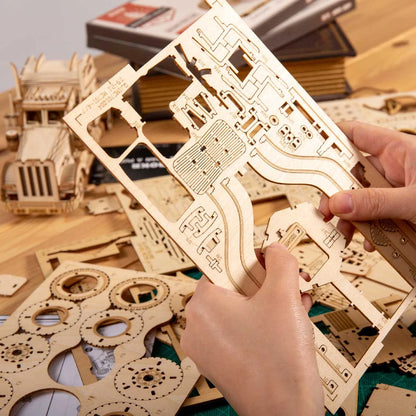 Mains détachant les pièces prédécoupées des planches en bois du puzzle 3D L'Héritage Automobile