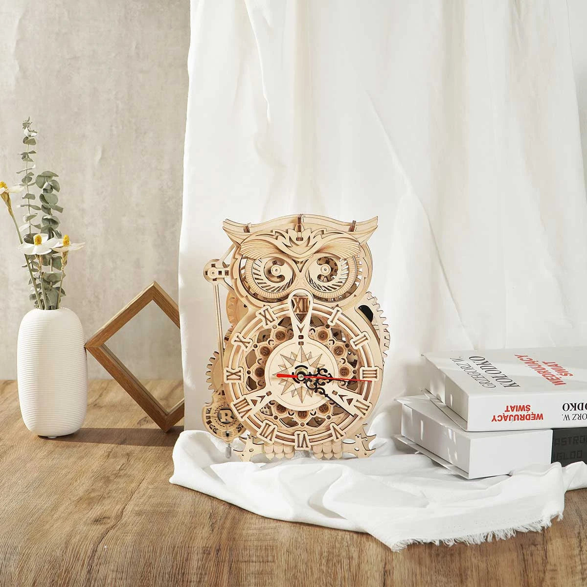 Horloge hibou en bois sur un bureau clair avec livres et lin blanc
