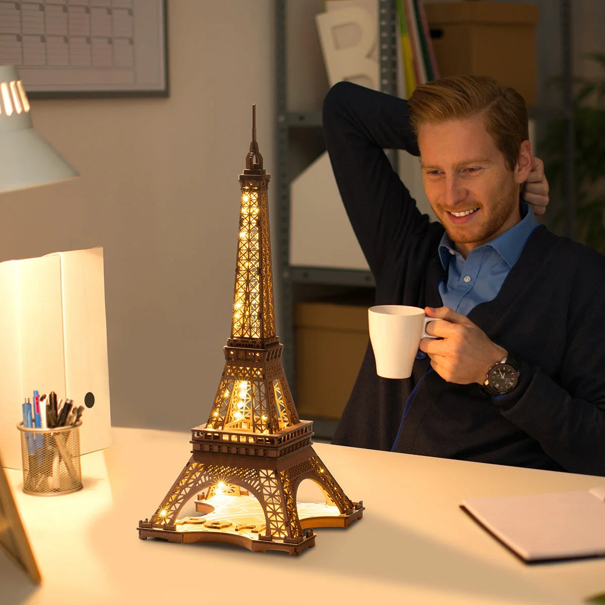 Tour Eiffel lumineuse en bois sur un bureau à côté d'un homme buvant un café
