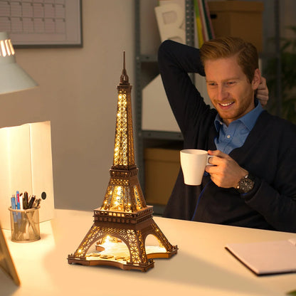Tour Eiffel lumineuse en bois sur un bureau à côté d'un homme buvant un café
